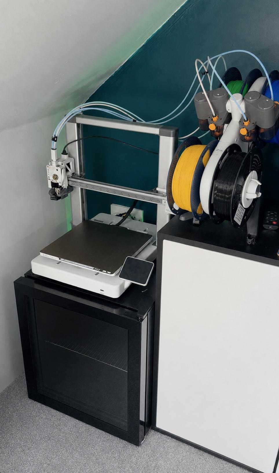Bambu Lab A1 and AMS Lite installed on two cabinets in a home room, with four PTFE filament tubes routed into the print head