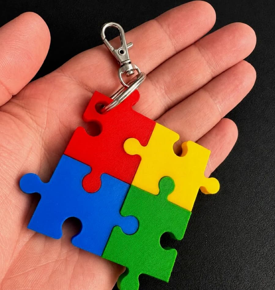A four-piece red, yellow, green and blue interlocking puzzle keyring resting in a hand