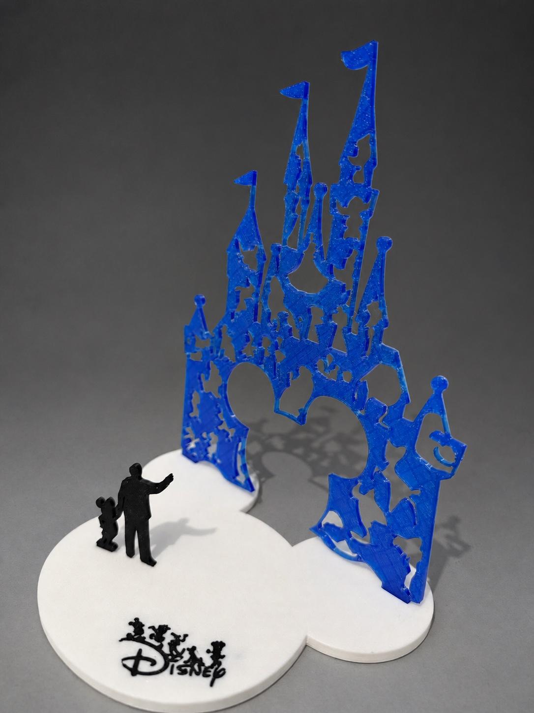 Blue 3D-printed castle display with thin towers and cut-out details on a white base beside two small black figures