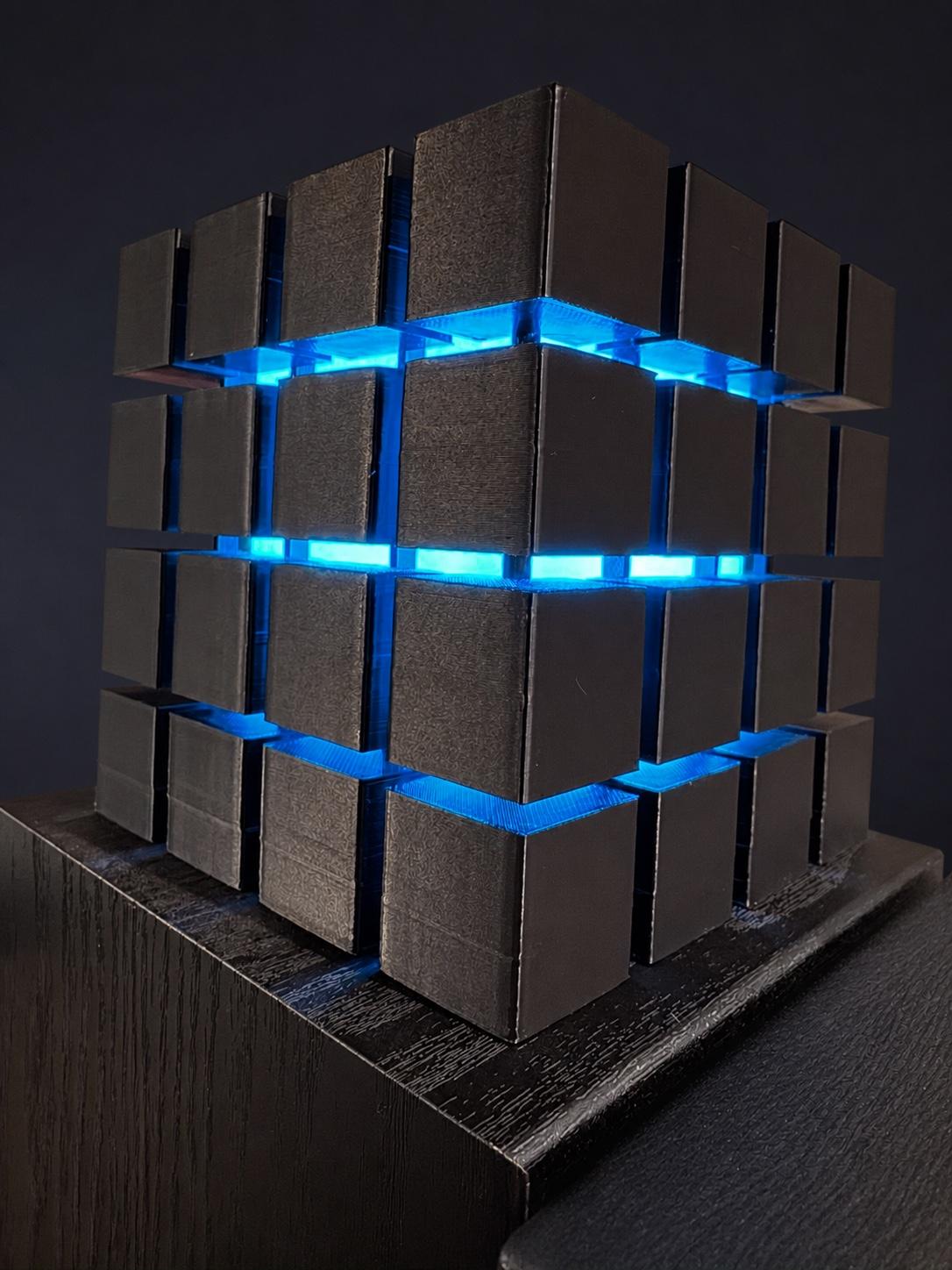 A black 3D-printed cube light glowing blue between its offset rows of square blocks