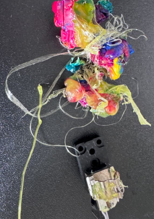 A removed A1 hotend component beside a large tangled mass of hardened rainbow filament